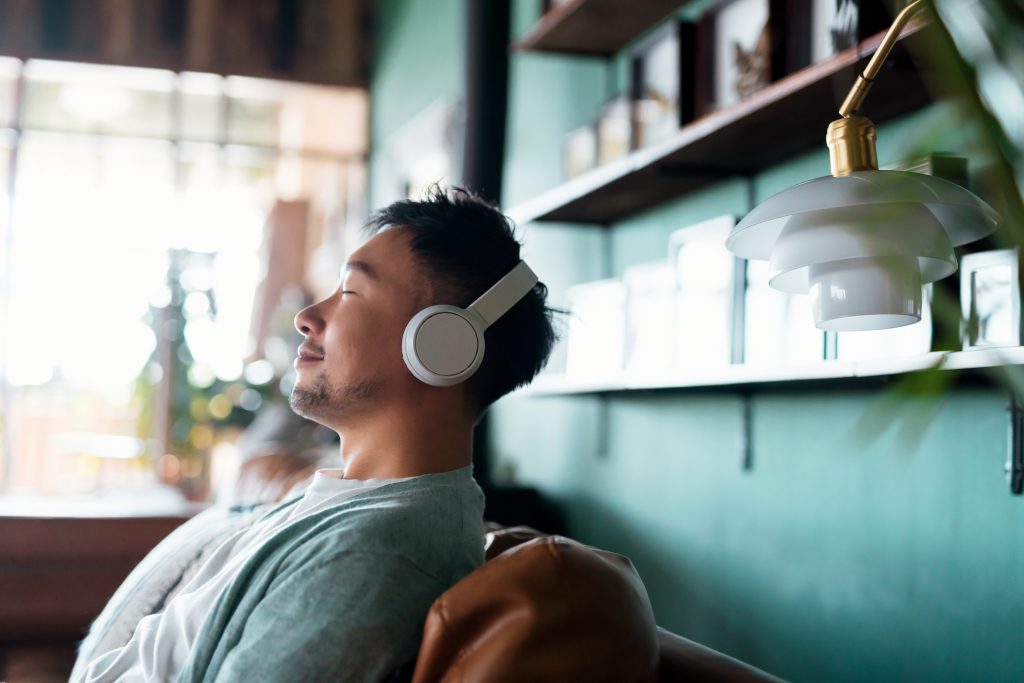 Young Asian man with eyes closed, enjoying meditating for his mental health with his headphones